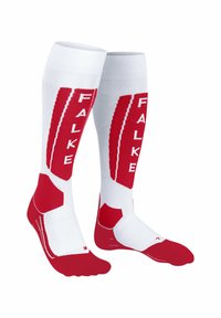 Calze bianche alte fino al ginocchio con accenti rossi, caratterizzate da un motivo a zigzag e il nome del brand "FALKE" stampato verticalmente su entrambi i lati.