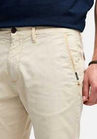 Beige katoenmengsel broek met knoopsluiting, zijzak en subtiele textuur. Een logotag is zichtbaar op de zijnaad.