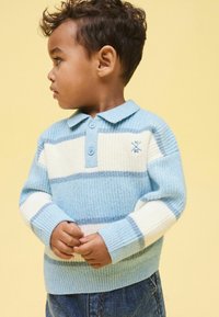 Vaaleansininen neulottu villapaita valkoisilla raidoilla, jossa on kaulus ja kaksi nappia, yhdistetty farkkuihin. Pehmeä, teksturoitu kangas.