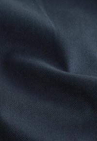 Dunkelnavyblauer Stoff mit feiner diagonaler Rippstruktur und subtilen Falten, die weiche Schatten und Highlights erzeugen.