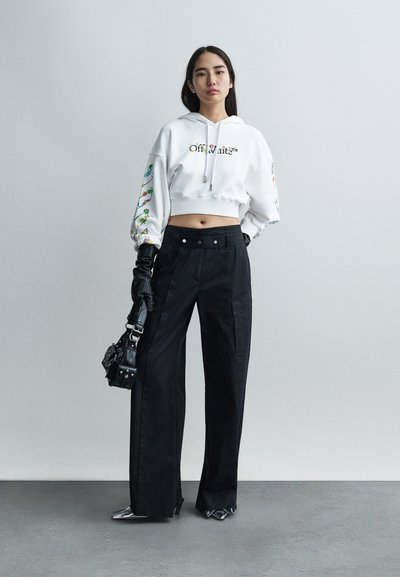 Λευκό cropped hoodie με πολύχρωμη κεντητική στα μανίκια, σε συνδυασμό με μαύρο cargo παντελόνι ψηλόμεσο. Γυαλιστερά μαύρα γάντια και μυτερά παπούτσια.