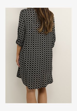 Robe à motif noir et blanc avec une coupe ample, des manches trois-quarts et un ourlet arrondi, confectionnée dans un tissu léger. Motif géométrique remarquable.