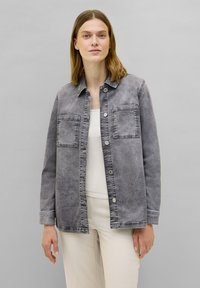Giubbotto in denim grigio con chiusura a bottoni, due tasche sul petto e colletto. Il tessuto presenta una texture sbiadita e cuciture a contrasto.