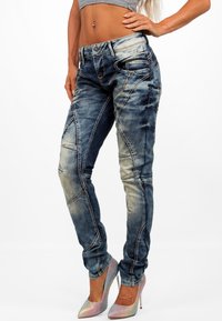 Jeans in denim blu aderenti con dettagli strappati, cuciture a contrasto e un design a gamba affusolata. Abbinati a tacchi alti luccicanti.