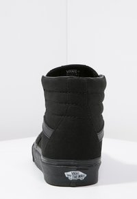 Adidași negri tip gheată din pânză, cu un superior texturat, dungi contrastante negre, guler căptușit și talpă din cauciuc cu un logo pe spate.