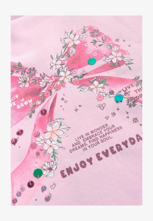 Ljusrosa tyg med en stor rosettdesign med blommönster, paljetter och tryckt text med uppmuntrande fraser.