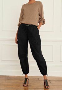Pantalon cargo noir avec des poignets élastiques, doté de poches latérales et d'une taille à cordon, associé à un pull en tricot texturé beige.