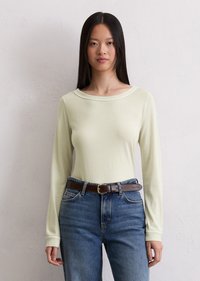 Lys grønn langermet topp med rund hals, sammen med blå denimjeans og et brunt lærbelte. Glatt tekstur, tettsittende stil.