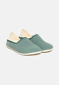 Green woven slippers with a smooth texture, beige accents, and a rounded toe design. Features a minimalist style and sturdy rubber sole.