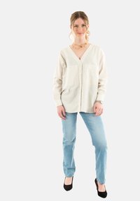 Leichte, gestreifte Shirtbluse in Beige und Weiß, mit langen Ärmeln und zwei Vordertaschen, kombiniert mit hellblauen Jeans und schwarzen High Heels.