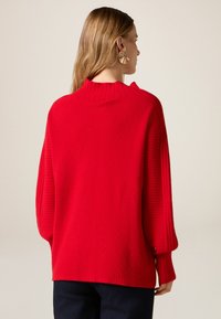 Maglione rosso lavorato a maglia con collo alto, texture a coste e vestibilità ampia. Presenta spalle scese e maniche oversize.