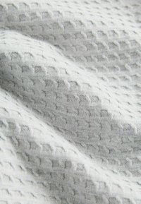 Strukturierter grauer Stoff mit einem Wabenmuster, das eine weiche, gestrickte Textur und subtile Farbnuancen aufweist.