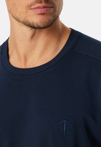 Námořnická modrá bavlněná tričko s kulatým výstřihem. Obsahuje jemně vyšívané logo na levé hrudi. Hladká textura s dobře padnoucím střihem.