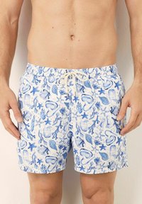 Costum de baie cu un fundal alb decorat cu motive marine în nuanțe de albastru, inclusiv stele de mare, scoici și echipament de scufundare. Talie elastică cu șnur.