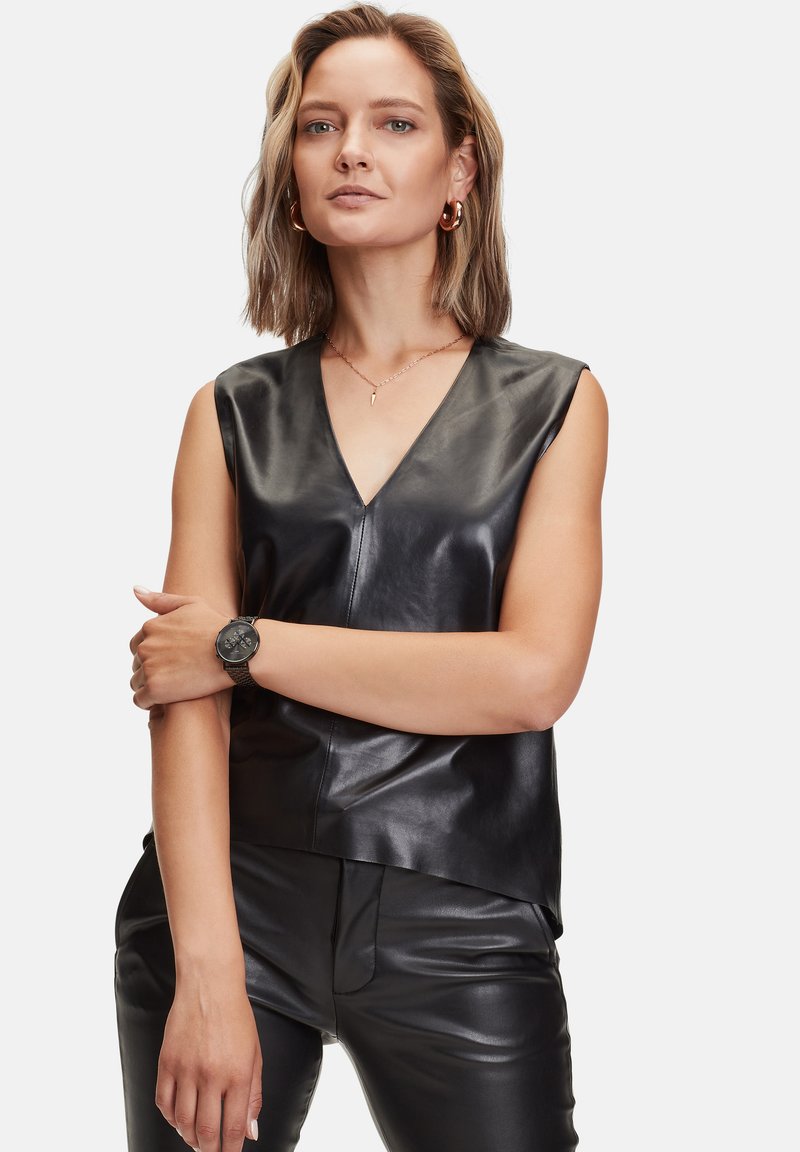 Zwart leren mouwloos topje met een v-hals en een gladde textuur, gecombineerd met zwarte leren broek en een zwart polshorloge.