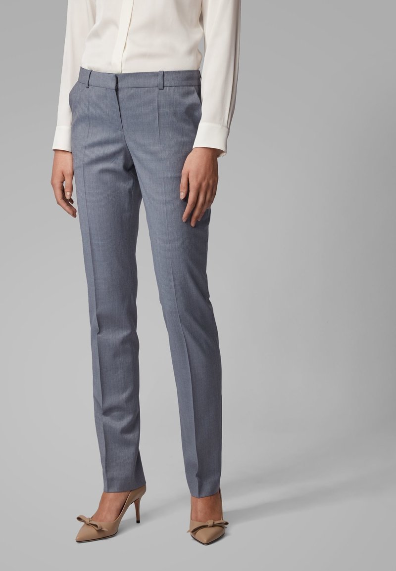Grijze geruite broeken met een getailleerde pasvorm, met een rits en zijzakken, gecombineerd met beige puntige hakken en een witte blouse.