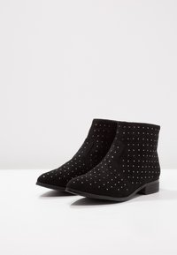 Botas de tobillo de ante negro con un patrón de puntos, tacón bajo, textura suave y elástico lateral para facilitar su uso.