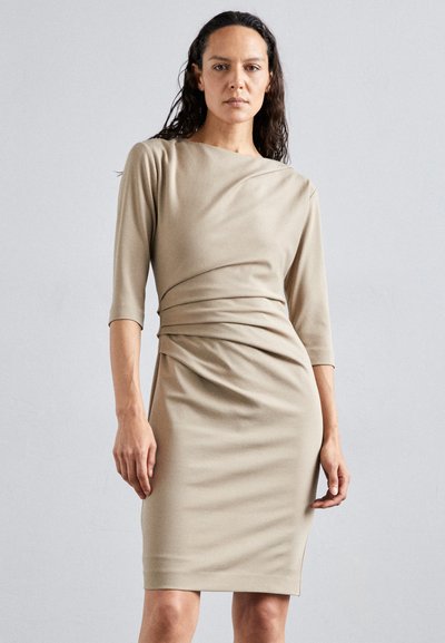 Beige tætsiddende kjole med trekvartærmer, drapering foran og glat tekstur. Enkel, minimalistisk design velegnet til formelle anledninger.