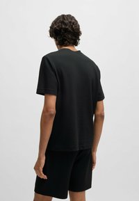 Zwart textuur T-shirt met korte mouwen, ronde hals en een relaxed fit, gecombineerd met bijpassende zwarte shorts, gezien vanachter.