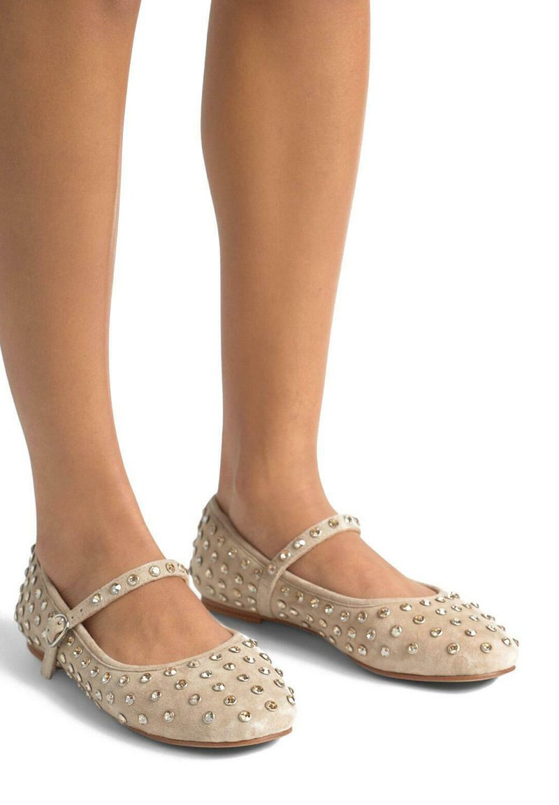 Bailarinas de ante beige con puntera redondeada, que cuentan con una correa en el empeine y decoradas con tachuelas decorativas de plata y oro.