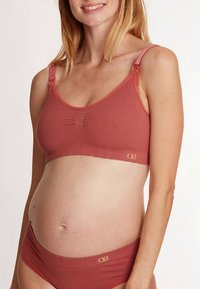 Soutien-gorge de maternité couleur corail doux, texture côtelée avec bretelles ajustables et détail de fronces subtil. À assortir avec des culottes taille basse coordonnées.