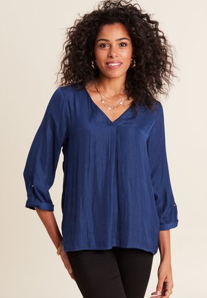 Marineblauwe, lichte blouse met een V-hals en driekwart mouwen, voorzien van opgerolde manchetten en een gladde, zijdezachte textuur.