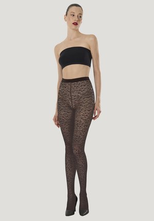 Kvinde iført gennemsigtige, sorte mønstrede strømpebukser, sort skulderfri bandeautop og sorte højhælede sko, stående mod en ensfarvet baggrund.