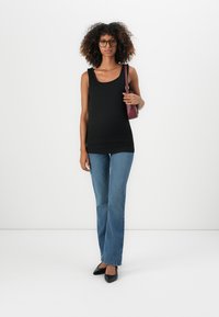 Top negro sin mangas con un escote redondo, acompañado de jeans acampanados de color azul claro. La modelo sostiene un bolso burdeos, lleva zapatos planos negros y gafas.