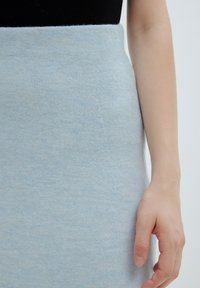 Lichtblauwe gebreide rok met een gladde textuur, hoge taille en een aansluitende pasvorm. Een hand rust tegen de rok, wat de natuurlijke huidtoon toont.