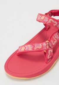 Rosa sandaler med en teksturert stropp som har et mønster i lys rosa og gult. Myk gummisåle med en liten kurve. Justerbar spenne.
