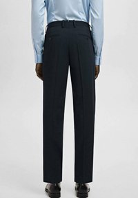 Ciemnoszare, dopasowane spodnie o prostym kroju nogawek, z dwoma tylnymi kieszeniami i subtelnymi zakładkami. Gładka tkanina, noszone z czarnymi butami.