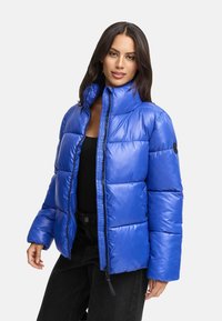 Kungblå puffjacka med hög krage, zip stängning och quiltad design. Har långa ärmar och en logotyp patch på vänster ärm.