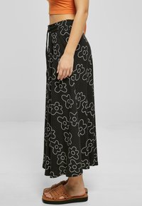 Black floral print maxi skirt with white flower design, elastic waistband, side slit, and a flowy silhouette. Paired with brown slide sandals.