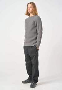Grauer, gerippter Strickpullover mit Rundhalsausschnitt, kombiniert mit schwarzen, lockeren Hosen und dunklen Schuhen. Schlichtes, strukturiertes Design ohne Muster.