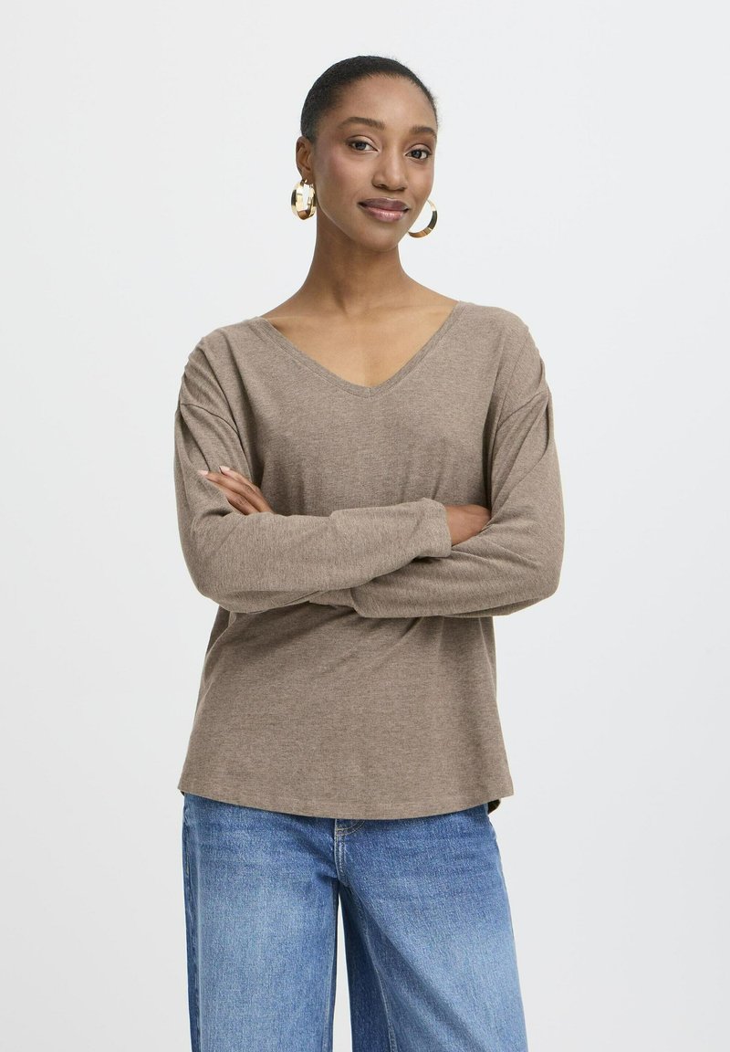 Brauner V-Ausschnitt-Pullover mit langen Ärmeln, entspannter Schnitt, weicher Textur. Kombiniert mit hellblauen Jeans, zeigt einen lässigen Look.
