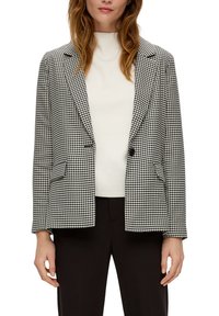 Schwarz-weißer Hahnentrittmuster-Blazer mit strukturiertem Design, einreihiger Knopfverschluss, geschlitzte Revers und zwei Fronttaschen. Trägt man über einem weißen Oberteil.