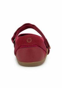 Scarpa rossa con tomaia in tessuto morbido, cinturino regolabile e suola in gomma. Presenta un logo circolare impresso sul retro.