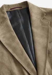 Blazer en daim marron avec un col cranté, dotée d'une doublure à motif noir et d'un petit détail de poche avant. Texture lisse dans l'ensemble.