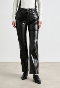 Pantalons droits en fausse cuir noir avec une finition brillante, dotés de poches avant et d'une taille haute, associés à des sabots.