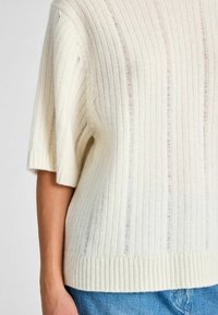 Tejkrémszínű, bordázott kötött felső rövid ujjal. Puha tapintása van, laza fazonú, és vastagabb bordázott szegéllyel rendelkezik alul.