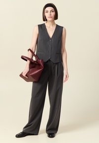 Grått väst med ränder och knappar, kombinerat med löst sittande grå byxor. Håller en bordeauxfärgad läderhandväska. Slät yta och skräddarsydd passform.