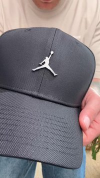 Căciulă de baseball neagră, realizată dintr-un material texturat, având un logo Jumpman alb pe față. Designul include un vârf curbat și o formă bine definită.