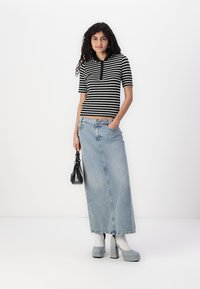 Strippet svart og hvitt t-skjorte med korte ermer, kombinert med et langt, lys blått denimskjørt. Grå plattformhæler og en liten svart håndveske fullfører looken.