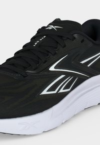Μαύρο αθλητικό sneaker με λευκή σόλα και λευκό λογότυπο Reebok, με μαύρα κορδόνια και υφασμάτινο ανώτερο υλικό.