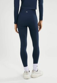 Granatowe elastyczne legginsy z wysokim stanem, z teksturowanymi panelami po bokach i detalu z logo z tyłu, w połączeniu z białymi trampkami.