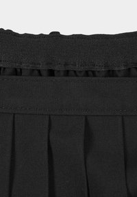 Falda negra con pliegues y cintura elástica. La tela parece tejida, con una textura suave y un brillo sutil. Acentos de volantes en la parte superior.