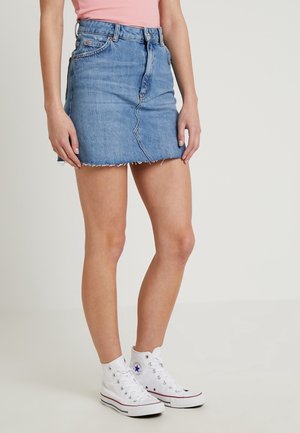 Lichtblauwe denimrok met een rafelrand, hoge taille, vijf zakken en riemlussen, gecombineerd met witte hoge sneakers.