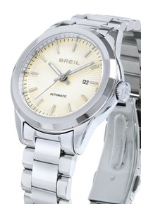 Montre automatique en argent avec un cadran jaune texturé, index heures en argent, guichet de date à 3 heures et un bracelet en métal poli.