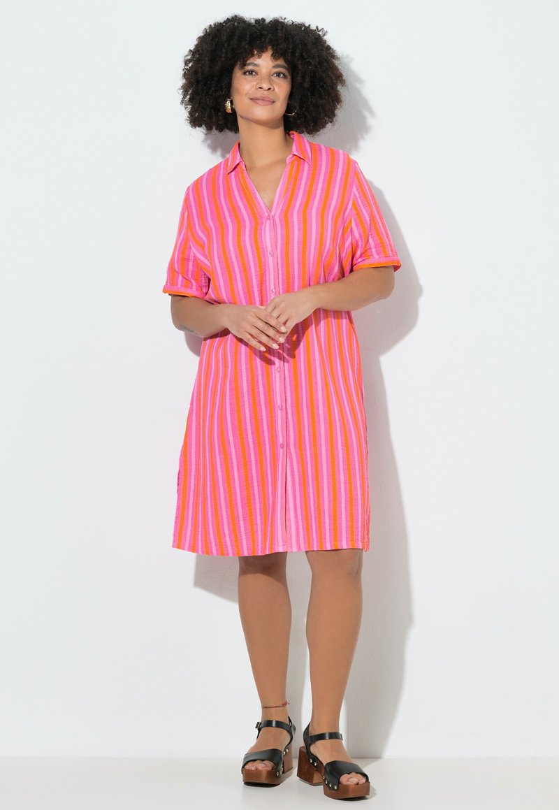Femme debout portant une robe à boutons rayée rose, orange et rouge à manches courtes, et des sandales à plateforme noires.