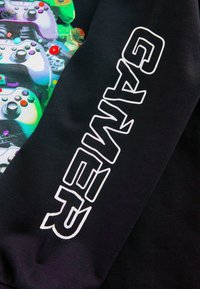 Schwarzer Sweatshirt mit einem bunten Grafik von Videospielcontrollern und dem Wort "GAMER" in fetter weißer Schrift entlang des Ärmels.